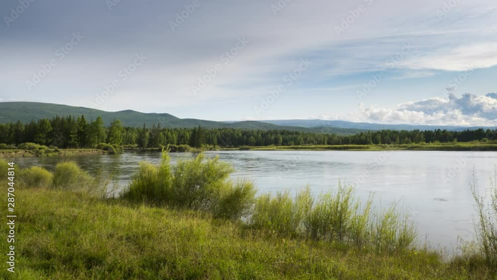 Timelapse. Autumn landscape of fast flowing river with green grass and high mountains in fine sunny weather with moving clouds in the blue sky Timelapse. Autumn landscape of fast flowing river with green grass and high mountains in fine sunny weather with moving clouds in the blue sky