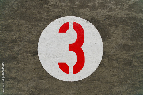 Red number three inside white circle painted on concrete