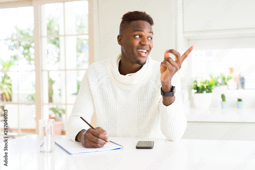 African american student man writing on a paper using a pencil very happy pointing with hand and finger to the side African american student man writing on a paper using a pencil very happy pointing with hand and finger to the side