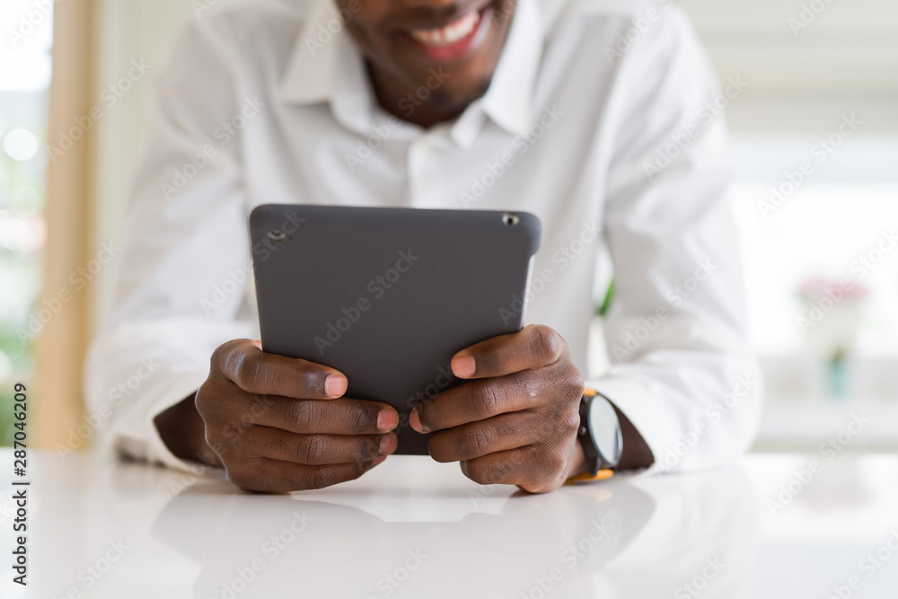 Close up of african business man using touchpad tablet, working sitting on a desk smiling Close up of african business man using touchpad tablet, working sitting on a desk smiling
