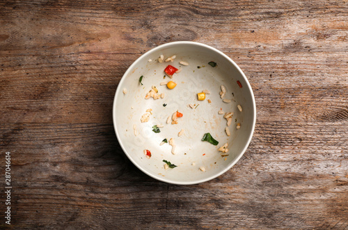Dirty bowl with food leftovers on wooden background, top view