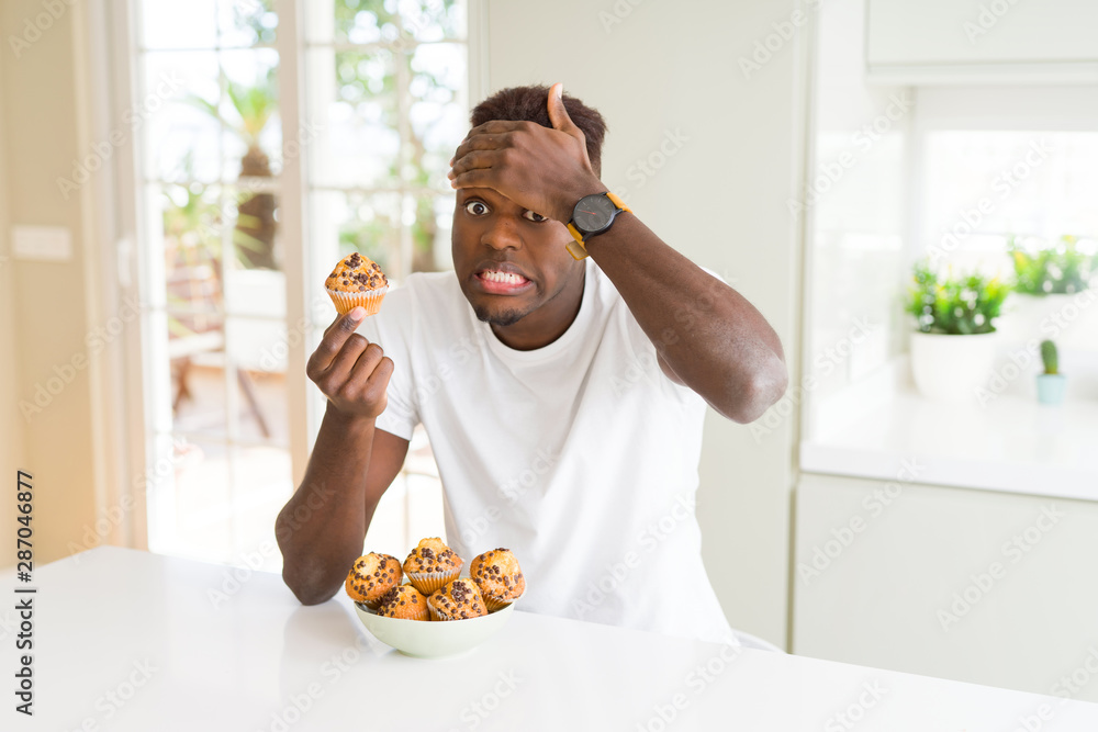 African american man eating chocolate chips muffin stressed with hand