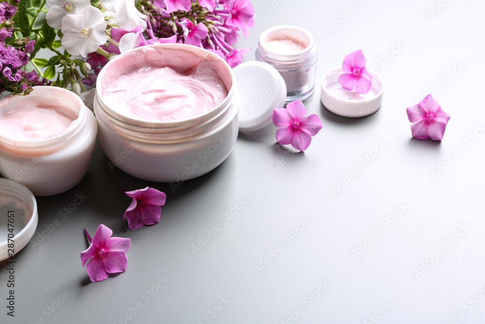 Jars of body cream and flowers on grey background. Space for text Jars of body cream and flowers on grey background. Space for text