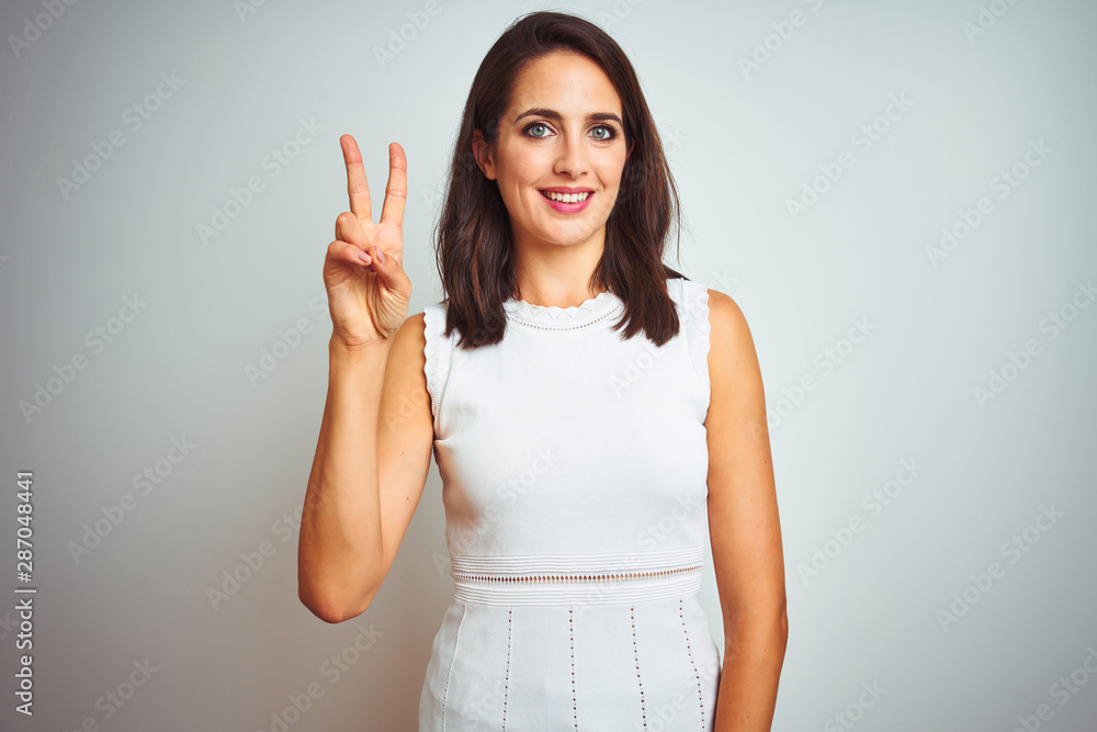 Young beautiful woman wearing dress standing over white isolated background showing and pointing up with fingers number two while smiling confident and happy. Young beautiful woman wearing dress standing over white isolated background showing and pointing up with fingers number two while smiling confident and happy.