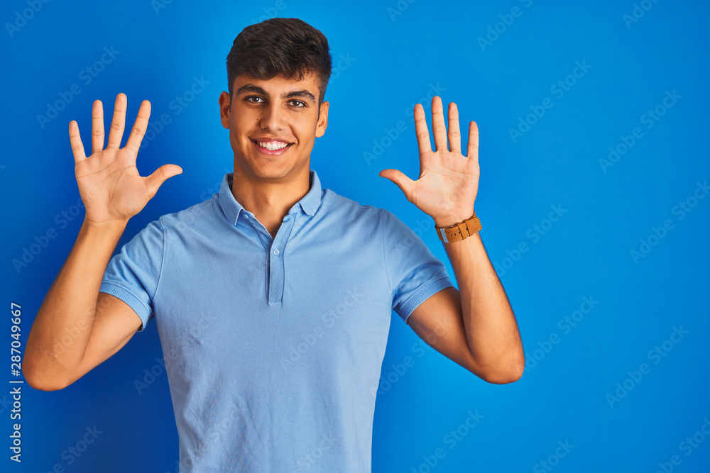 Young indian man wearing casual polo standing over isolated blue background showing and pointing up with fingers number ten while smiling confident and happy. Young indian man wearing casual polo standing over isolated blue background showing and pointing up with fingers number ten while smiling confident and happy.