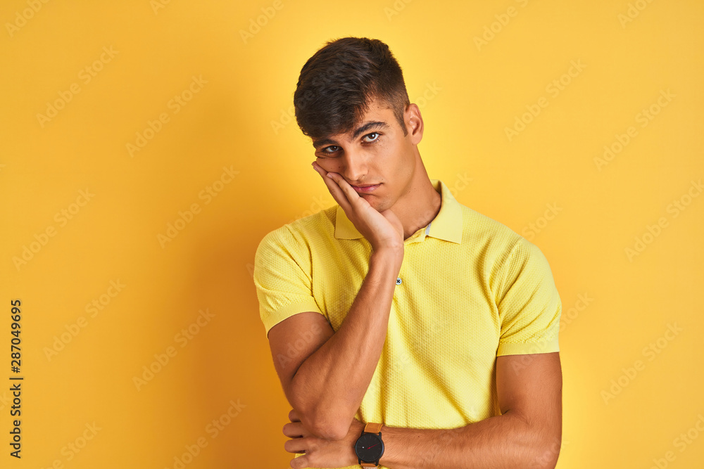 Young indian man wearing casual polo standing over isolated yellow background thinking looking tired and bored with depression problems with crossed arms. Young indian man wearing casual polo standing over isolated yellow background thinking looking tired and bored with depression problems with crossed arms.
