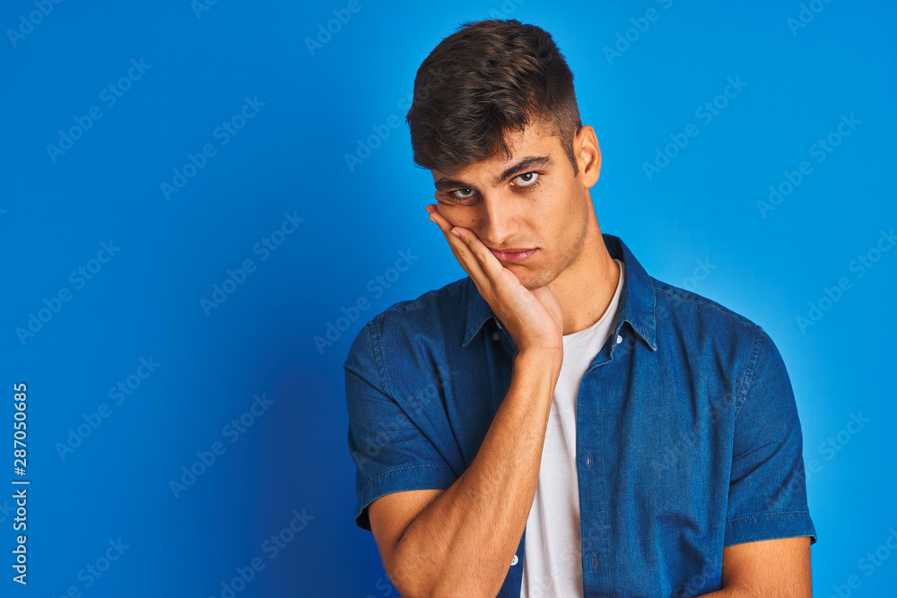 Young indian man wearing shirt standing over isolated blue background thinking looking tired and bored with depression problems with crossed arms. Young indian man wearing shirt standing over isolated blue background thinking looking tired and bored with depression problems with crossed arms.