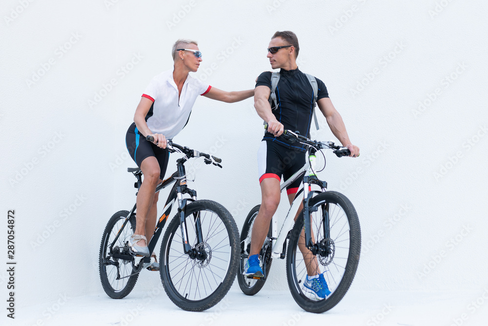 Man and woman with bicycles, a woman holds a man by the shoulder, on a light background.