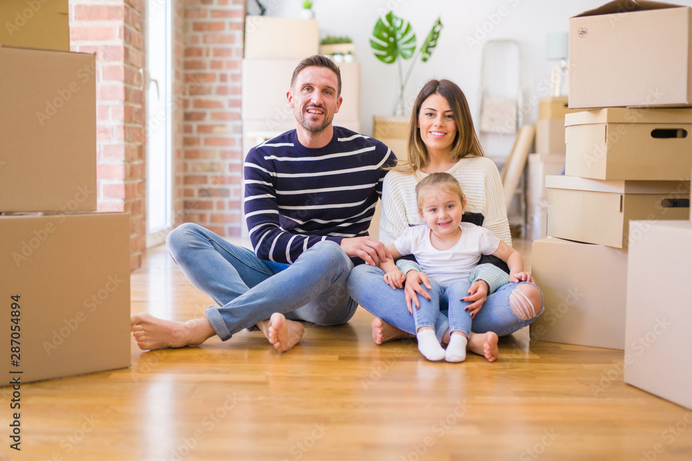 Beautiful family sitting on the floor playing with his kid at new home around cardboard boxes