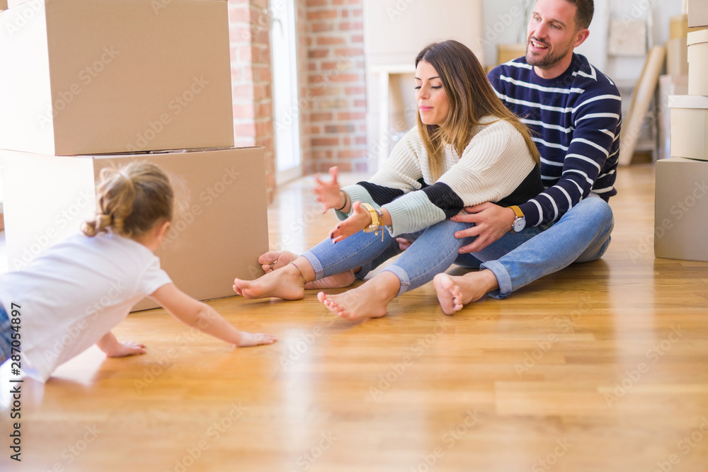 Beautiful family sitting on the floor playing with his kid at new home around cardboard boxes