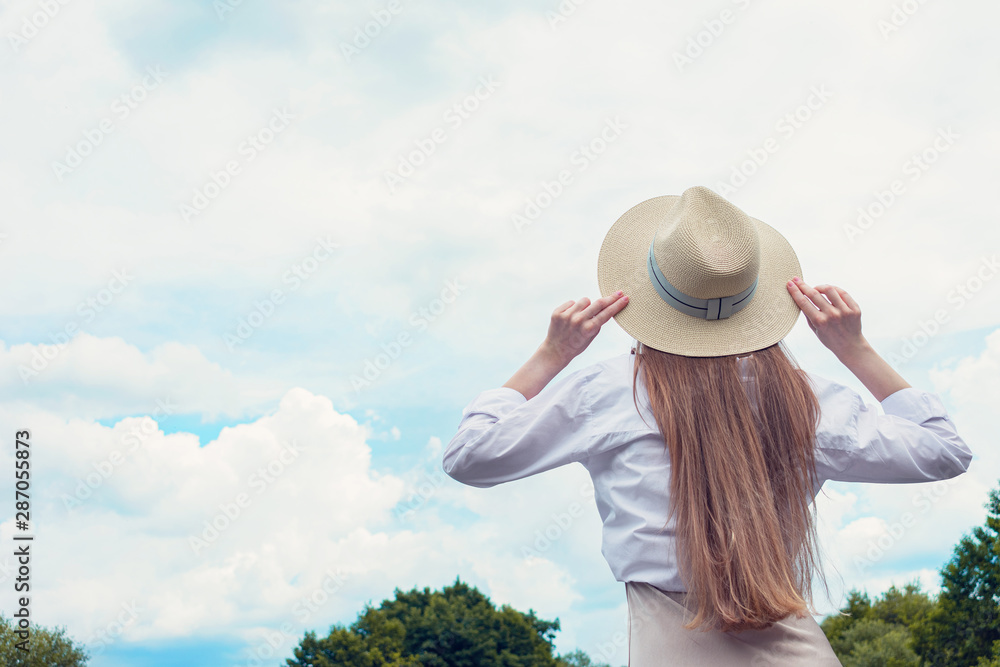 Beauty woman in a hat travels the world, girl looks at the beautiful lake and keeps her hat from the wind, back view, copy space, toned
