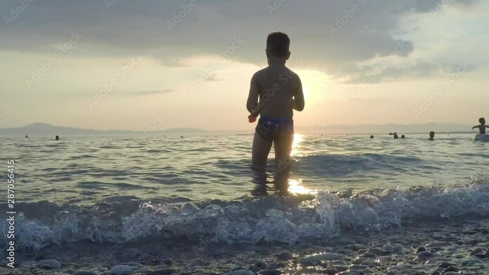 Kid plays at the waves with sunset on the background at Kalamata beach, Greece