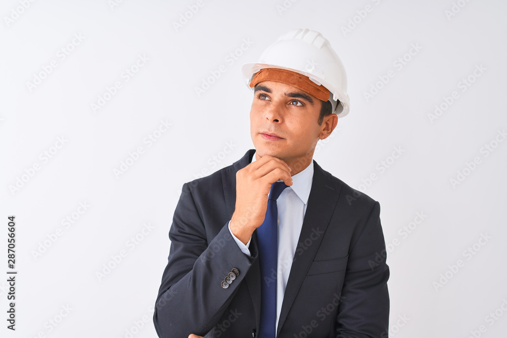 Young handsome architect man wearing suit and helmet over isolated white background with hand on chin thinking about question, pensive expression. Smiling with thoughtful face. Doubt concept. Young handsome architect man wearing suit and helmet over isolated white background with hand on chin thinking about question, pensive expression. Smiling with thoughtful face. Doubt concept.