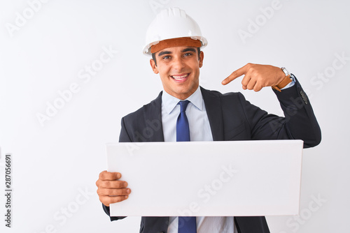 Young handsome architect man wearing helmet holding banner over isolated white background with surprise face pointing finger to himself