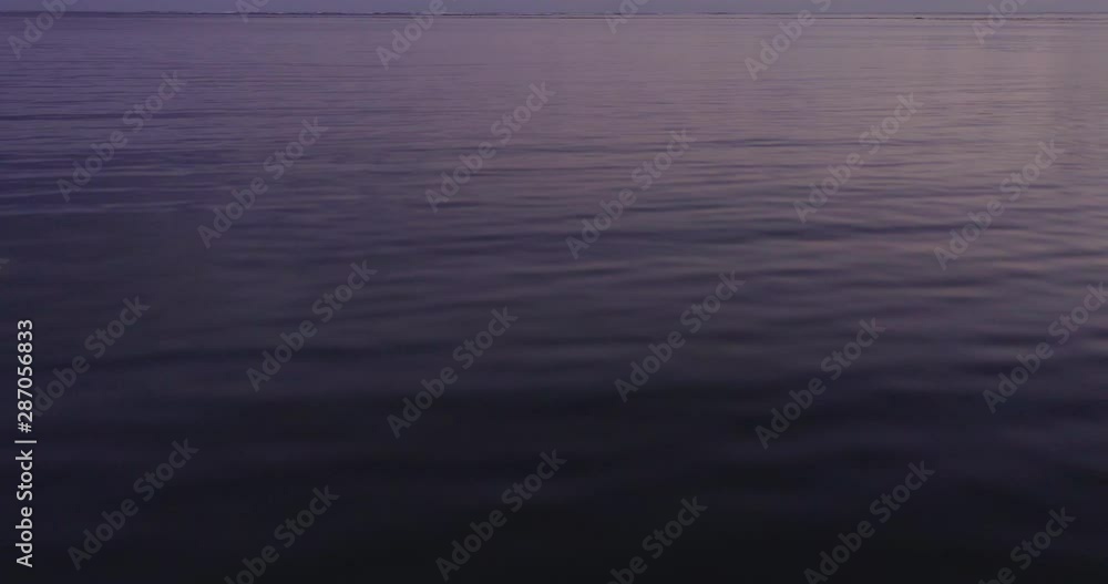 Flying over calm purple ocean at dusk