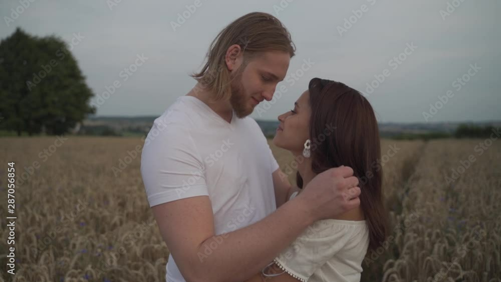 Medium cinematic slow motion handheld shot of a romantic mixed race couple standing in the middle of a hay wheat spike field kissing and holding each other and turning around passionately Medium cinematic slow motion handheld shot of a romantic mixed race couple standing in the middle of a hay wheat spike field kissing and holding each other and turning around passionately