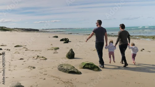 Parents with twins walking hand-in-hand down beautiful secluded beach, sunny day photo