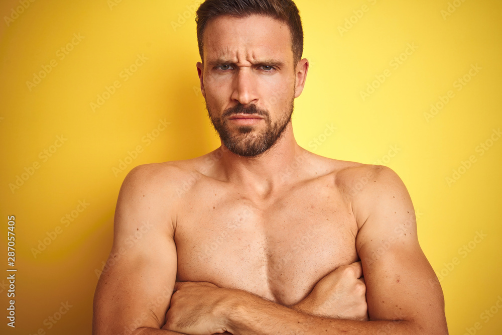 Sexy young shirtless man showing nude fitness chest over yellow isolated background skeptic and nervous, disapproving expression on face with crossed arms. Negative person.