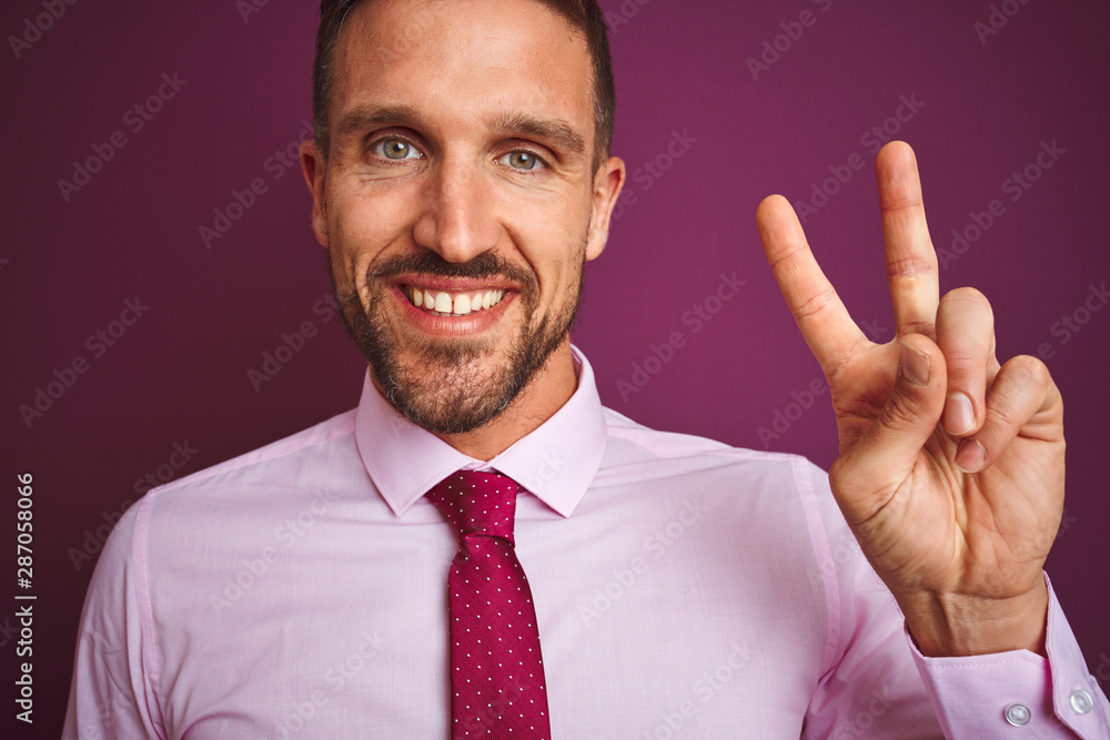 Close up of business man wearing elegant shirt and tie over purple isolated background smiling with happy face winking at the camera doing victory sign. Number two. Close up of business man wearing elegant shirt and tie over purple isolated background smiling with happy face winking at the camera doing victory sign. Number two.