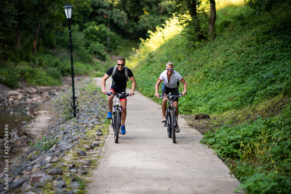 A man and a woman on bikes ride along a path in a park.