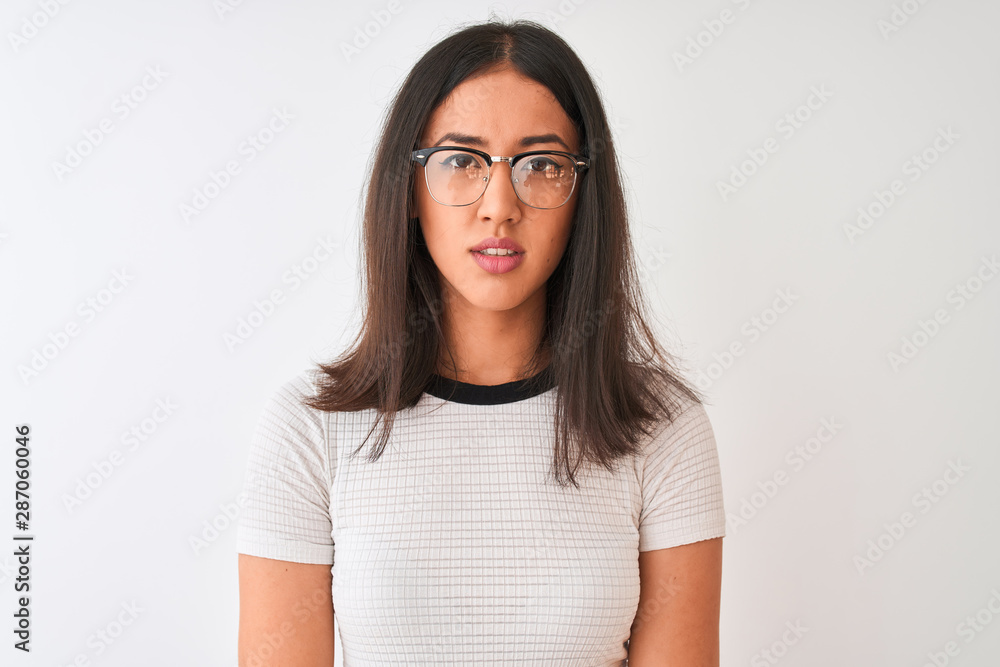 Chinese woman wearing casual t-shirt and glasses standing over isolated white background with serious expression on face. Simple and natural looking at the camera. Chinese woman wearing casual t-shirt and glasses standing over isolated white background with serious expression on face. Simple and natural looking at the camera.