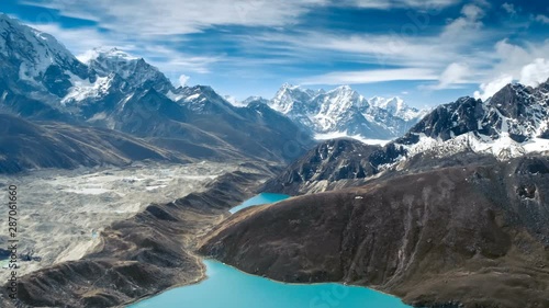 Calm Blue Gokyo Lake surrounded by bare rocky hills against high mountains with snow on slopes upper view. Travel, landscape, holiday, recreation. Himalaya, Nepal. Slow motion, parallax, time lapse 4K photo