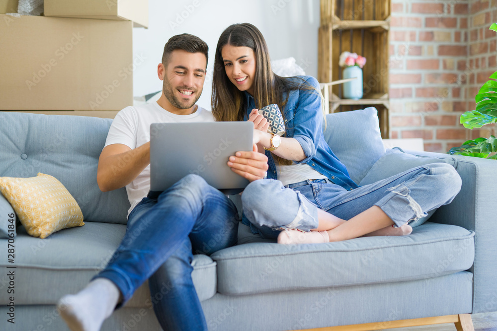Young couple moving to a new home relaxing sitting on the sofa using computer laptop, smiling happy for moving to new apartment Young couple moving to a new home relaxing sitting on the sofa using computer laptop, smiling happy for moving to new apartment