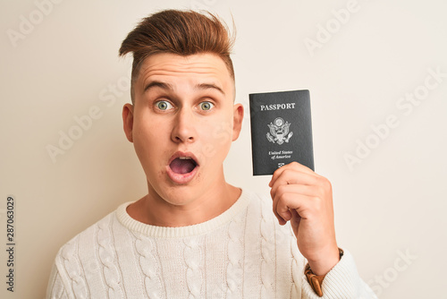Young handsome man holding USA United States passport over isolated white background scared in shock with a surprise face, afraid and excited with fear expression