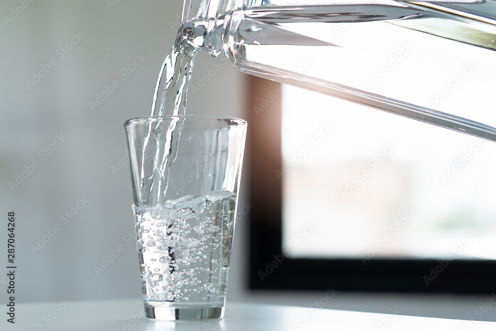 Fototapeta kobieta wylewa wodę mineralną do szklanki.