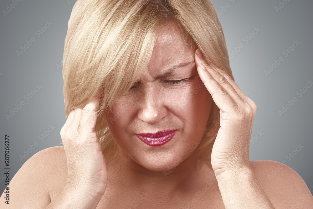 A tired upset middle-aged woman suffers from severe chronic headache, migraine, dizziness, during menopause. Concept of zhesky health. A tired upset middle-aged woman suffers from severe chronic headache, migraine, dizziness, during menopause. Concept of zhesky health.