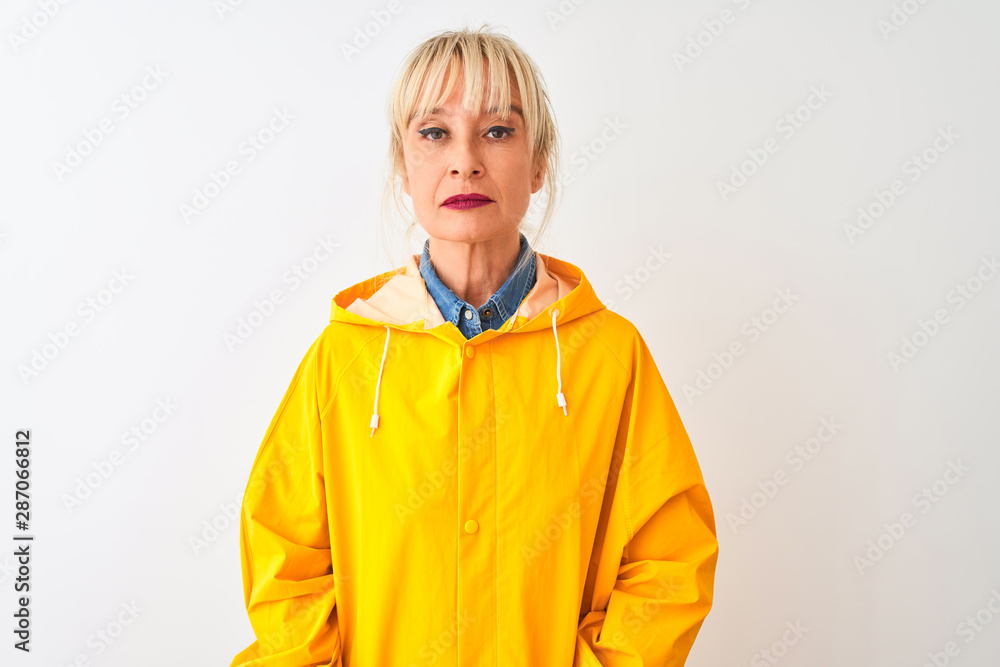 Middle age woman wearing yellow rain coat standing over isolated white background with serious expression on face. Simple and natural looking at the camera.