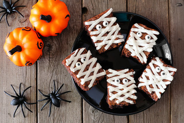Halloween mummy brownies, above view with decor on a rustic wood background