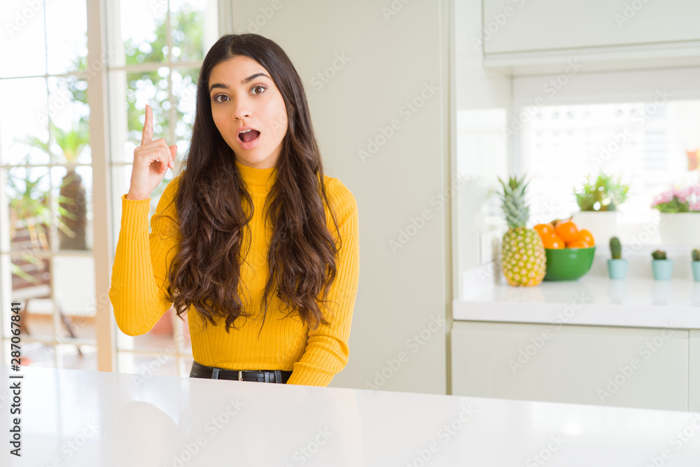 Young beautiful woman at home on white table pointing finger up with successful idea. Exited and happy. Number one. Young beautiful woman at home on white table pointing finger up with successful idea. Exited and happy. Number one.