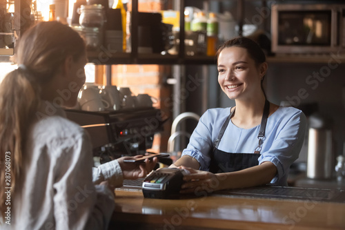 Female customer pay with phone on nfc with smiling barista photo