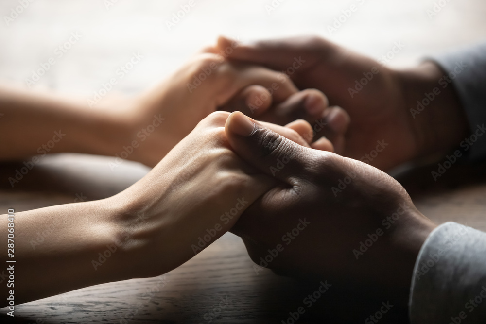 Mixed ethnicity couple holding hands on table, close up view - obrazy, fototapety, plakaty 