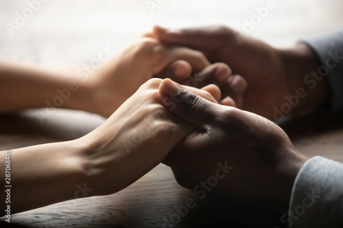 Mixed ethnicity couple holding hands on table, close up view