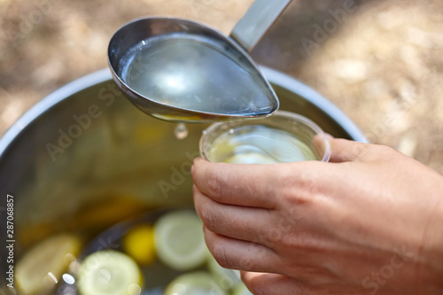 Process of pouring citrus lemonade from bucket in the forest for picnic