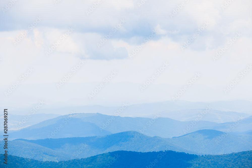 Naklejka premium Wspaniały krajobraz z niebieskimi sylwetkami wzgórz i gór z błękitnym niebem. tło