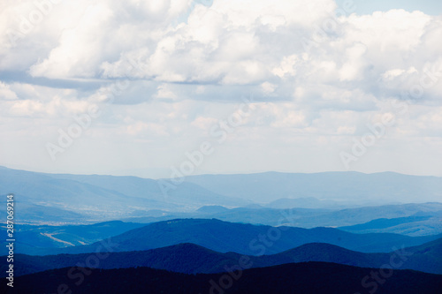 Landscape with blue silhouettes of mountains and clouds.