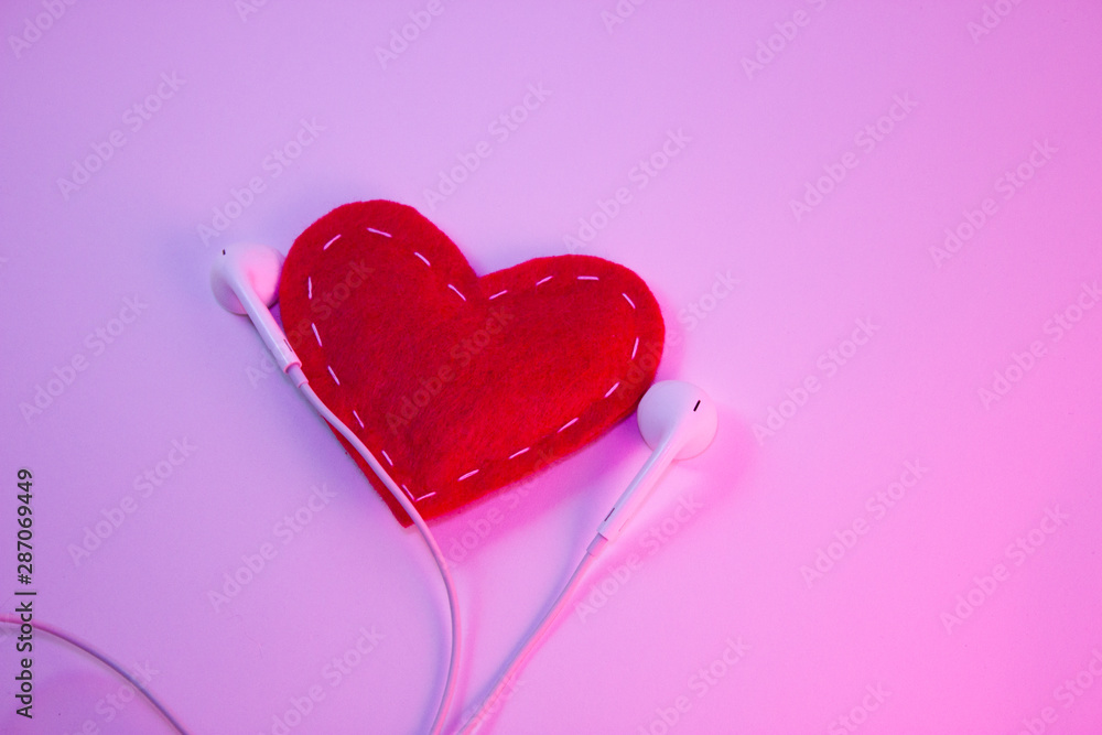 Red heart fabric with white threads and white headphones on a white background with pink light. Music concept, favorite music Red heart fabric with white threads and white headphones on a white background with pink light. Music concept, favorite music