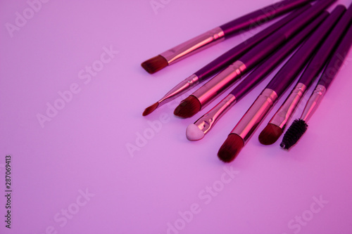 Makeup brushes with purple handle and orange hairs on white background, pink light