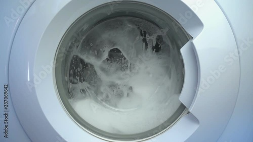 Close up view porthole of washing machine. Washing clothes process in slow motion.