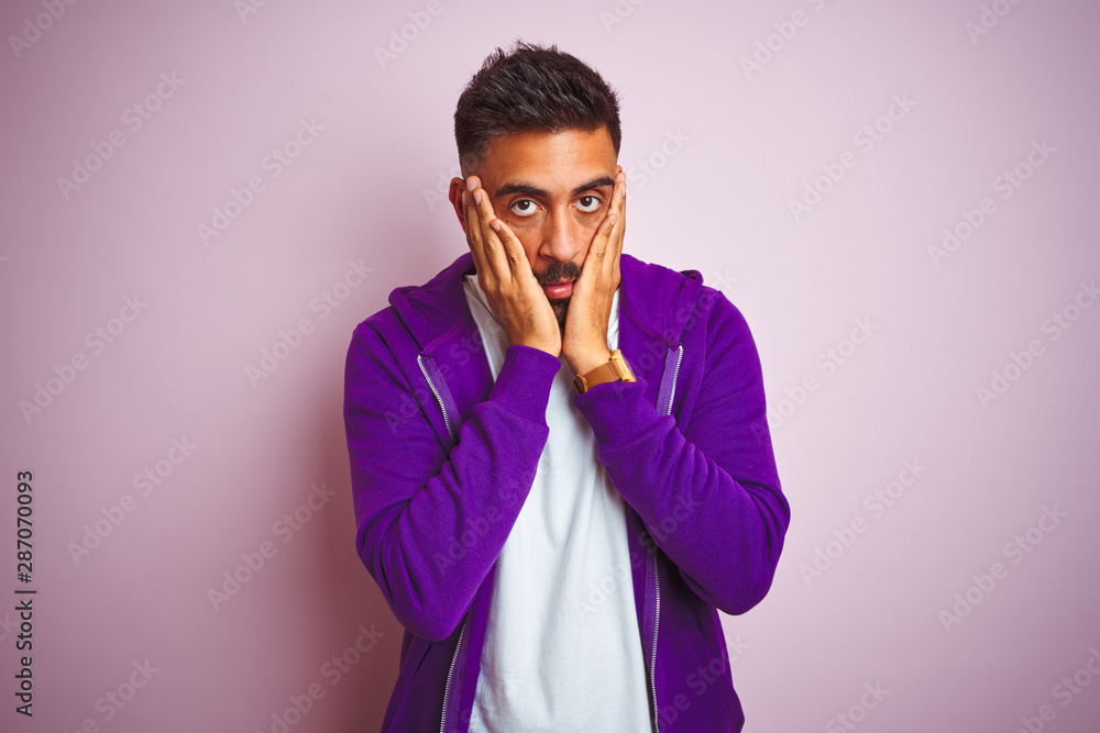 Young indian man wearing purple sweatshirt standing over isolated pink background Tired hands covering face, depression and sadness, upset and irritated for problem Young indian man wearing purple sweatshirt standing over isolated pink background Tired hands covering face, depression and sadness, upset and irritated for problem