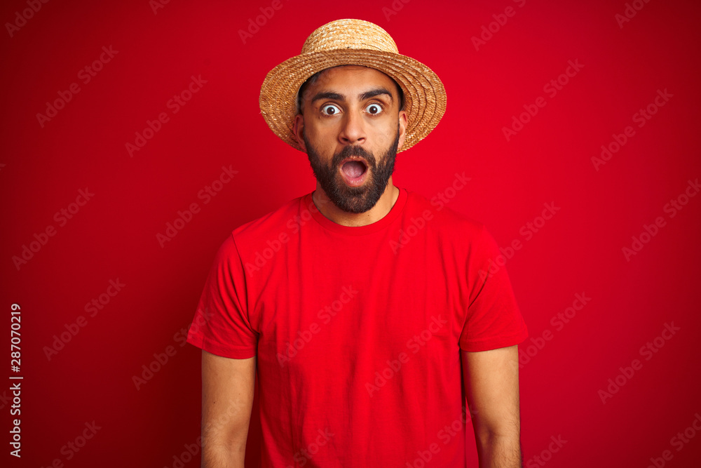 Young handsome indian man wearing t-shirt and hat over isolated red background afraid and shocked with surprise expression, fear and excited face.