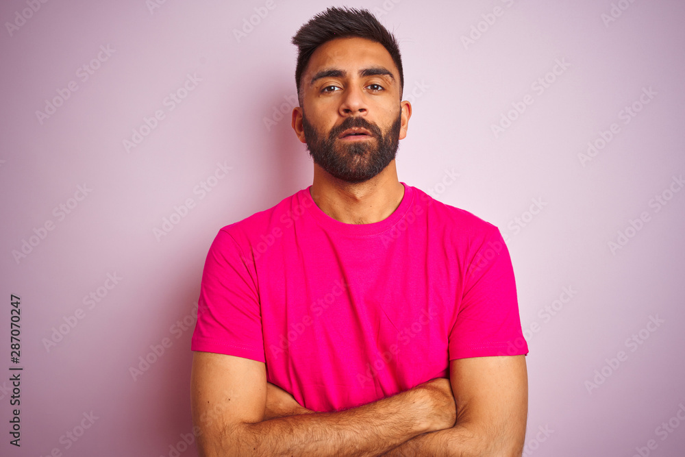Young indian man wearing t-shirt standing over isolated pink background skeptic and nervous, disapproving expression on face with crossed arms. Negative person. Young indian man wearing t-shirt standing over isolated pink background skeptic and nervous, disapproving expression on face with crossed arms. Negative person.