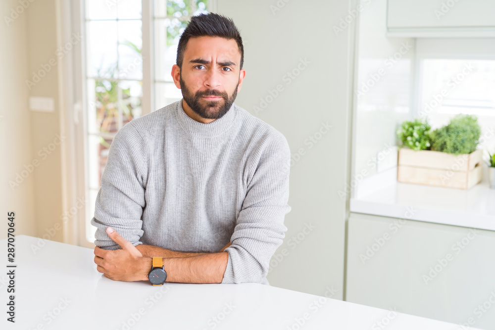 Handsome hispanic man wearing casual sweater at home skeptic and nervous, disapproving expression on face with crossed arms. Negative person. Handsome hispanic man wearing casual sweater at home skeptic and nervous, disapproving expression on face with crossed arms. Negative person.