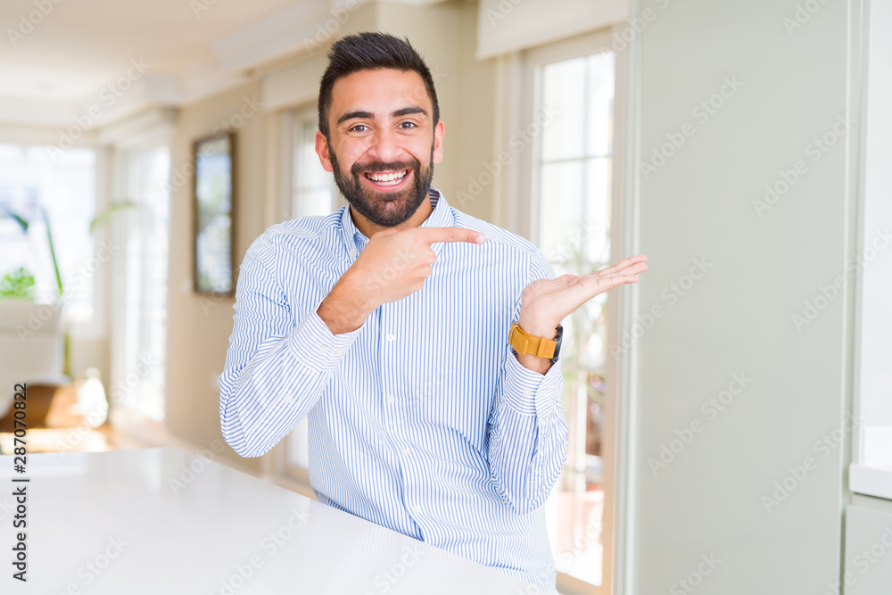 Handsome hispanic business man amazed and smiling to the camera while presenting with hand and pointing with finger.