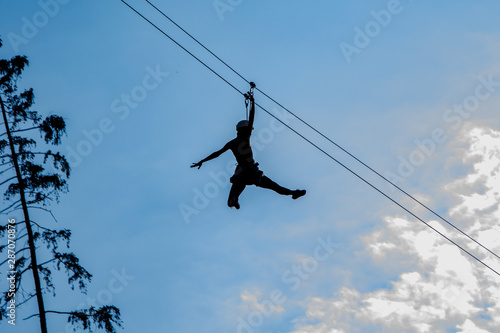 Silhouette girls down at speed straight angle to the cable or rope,Trolls and Zip Line against blue sky with clouds
