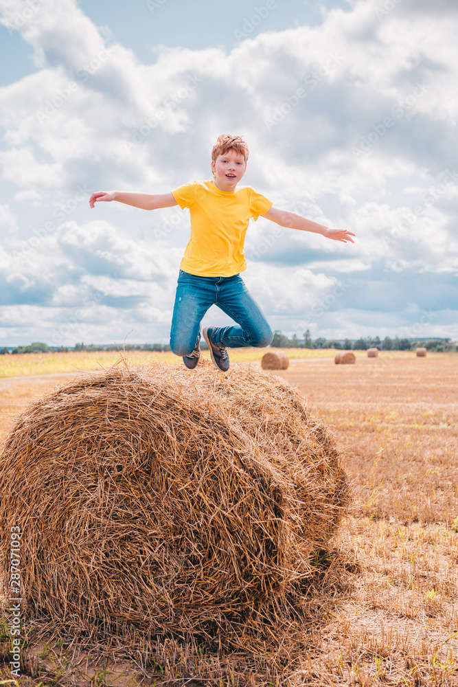 Red-haired Caucasian boy walks on a farm field among haystacks - wide angle and open aperture Red-haired Caucasian boy walks on a farm field among haystacks - wide angle and open aperture