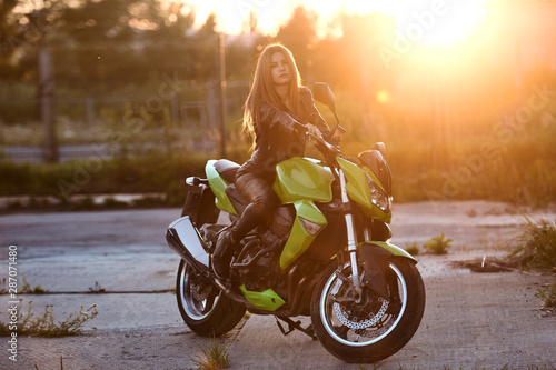 Beautiful young girl with a fashionable hairstyle and red lips poses next to motorcycle